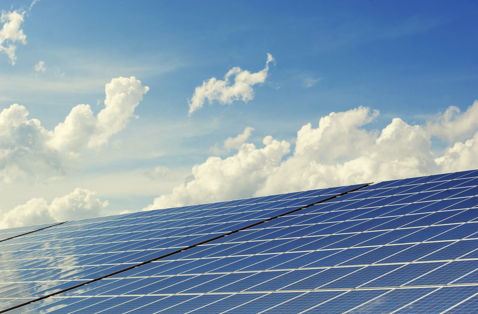 Solar panels angled toward a bright blue desert sky scattered with clouds