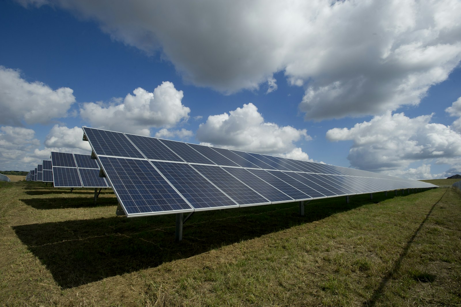 A ground-mounted solar array under a dramatic blue sky with sweeping clouds
